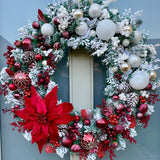 Decorative snowy Christmas wreath with red poinsettia, red, white and halogen berries, baubles and ornaments.