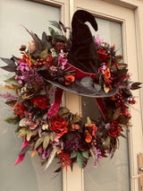 Halloween wreath with a witch hat and autumnal flowers on a door.
