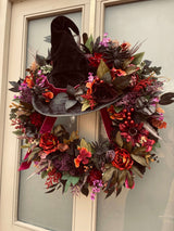 Halloween wreath with a witch hat and autumnal flowers on a door.