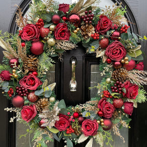 A large artificial Christmas wreath with a rich red color scheme, featuring various sizes of red and burgundy roses, pinecones, ferns, eucalyptus and hints of gold decorations. 60cm, reusable year after year.