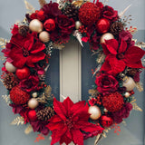 Decorative Christmas wreath with red flowers, gold leaves, and pinecones on a door.