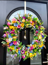 Bright multicolour artificial spring wreath with daffodils, tulips, and roses for front door decoration.
