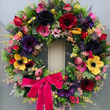 Luxury artificial large bright jewel tone anemone floral wreath with a pink ribbon on a door