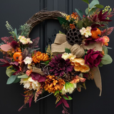 Autumn-themed wreath with colorful flowers and leaves on a black door.