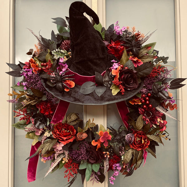 Halloween wreath with a black hat and autumnal flowers on a door.
