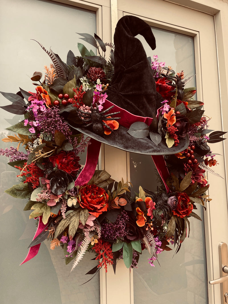 Halloween wreath with a witch hat and autumnal flowers on a door.