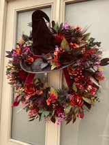 Halloween wreath with a witch hat and autumnal flowers on a door.