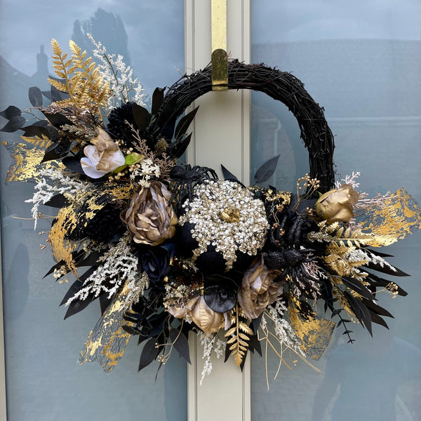 Decorative artificial Halloween wreath with black, gold, and white elements on a door.