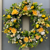 Floral wreath with yellow, white, and green flowers on a door.