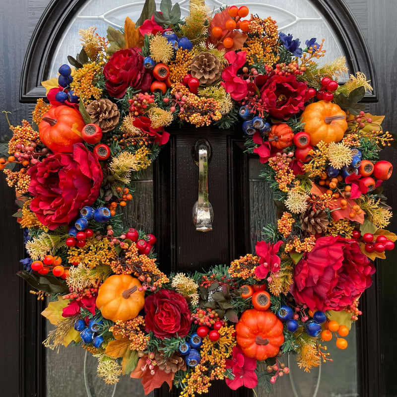 An extra large artificial autumn wreath showcasing an abundance of florals and berries in varying sizes and shades of reds, oranges and hints of dark blue. 