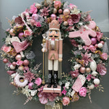 Artificial Christmas wreath with pink nutcracker at the centre with pink florals, baubles and sweeties.