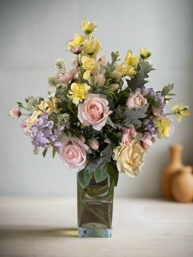 A tall, artificial hand tied flower bouquet in pastel shades of lemon, pink and lavender. Featuring roses, blossom, thistles and and hydrangea.