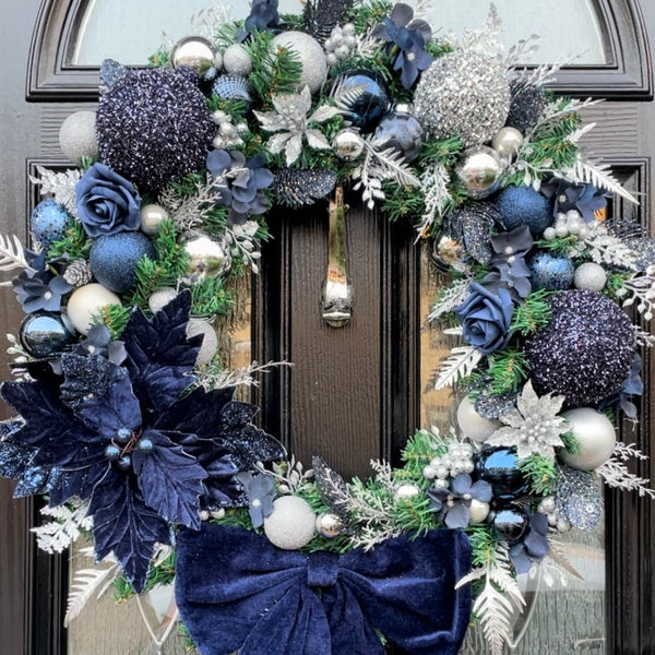 A large 65cm wreath featuring oversized glitter navy and silver baubles with navy roses and hydrangea throughout and silver flitter accents. Finished with a large navy velvet bow and poinsettia. 