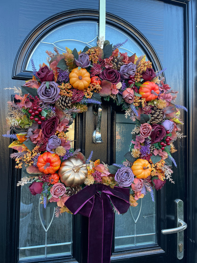 Luxury autumn wreath in shades of purple and orange, featuring roses, berries, pinecones and pumpkins 