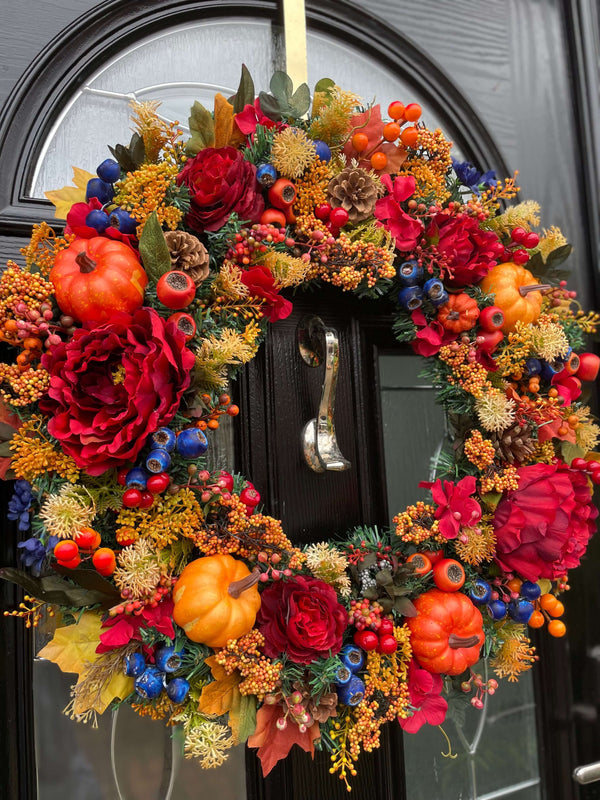 An extra large artificial autumn wreath showcasing an abundance of florals and berries in varying sizes and shades of reds, oranges and hints of dark blue. 