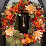 An extra large rustic orange autumn wreath with a green and hessian bow, adorned with berries, florals, and faux pumpkins, displayed on a door.